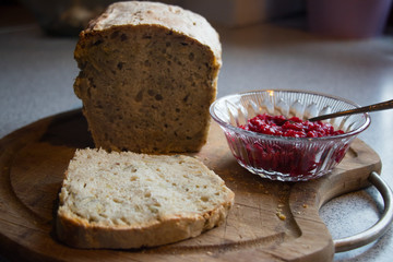 Homemade bread with pips lying on a wooden board with a glass bowl of homemade raspberry jam
