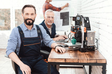 An engineer in a working overall posing in a technical laboratory. Behind it is a 3d printer.