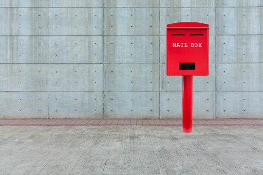 Red mail box on cement floor with white cement block wall as background