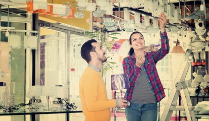 Fototapeta premium Smiling man and girl in lighter shop choosing stylish pendant lamp