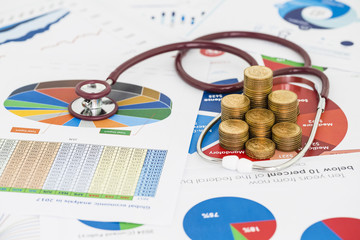 Stack of money coins with stethoscope checking are placed on the annual financial statements, concept of financial diagnosis