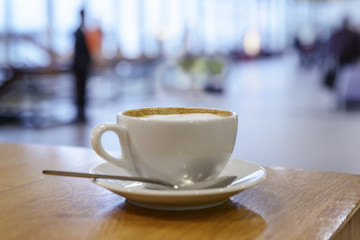cup of hot cappuccino coffee in a white cup is on the table in the airport lobby
