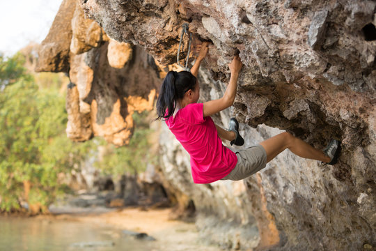 Young woman rock climber climbing on seaside cliff
