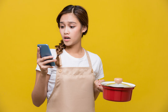 Young woman watching smart phone while cooking.