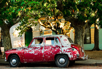 Old, rusty and red Car parked in a street under the trees