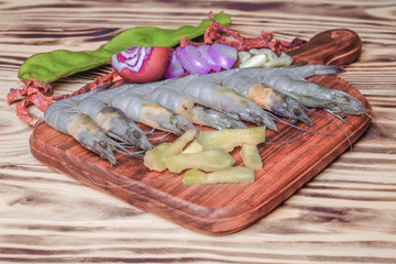 Fresh giant prawn on cutting board  with onion, garlic, petai, key lime, chilies, lemongrass, and ginger.