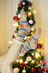 Fototapeta na wymiar Woman legs in woollen socks in front of Christmas tree.