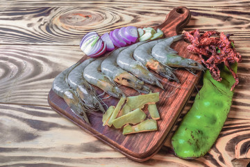 Fresh giant prawn on cutting board  with onion, garlic, petai, key lime, chilies, lemongrass, and...