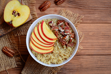 Simple quinoa porridge with topping. Diet quinoa porridge with fresh apples and pecan nuts in a white bowl and on wooden background with empty space for text. Rustic style. Top view