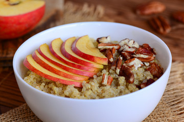 Sweet quinoa porridge with fruits and nuts. Vegan quinoa porridge with fresh apples and pecans in a white bowl. Rustic style. Closeup