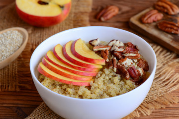 Quinoa porridge with fruits and nuts. Healthy quinoa porridge with fresh apples and pecans in a white bowl. Rustic style. Closeup