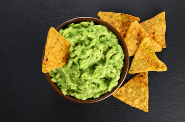 Bowl with guacamole and nachos on the background of a slate board.