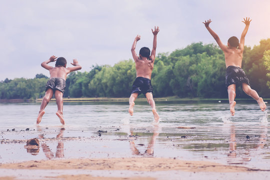 three asian young boys jumping into the lake.