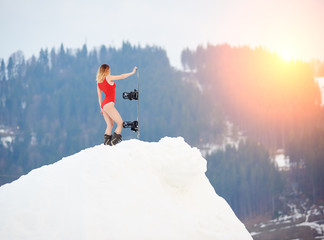 Hot woman snowboarder wearing red swimsuit, standing with snowboard on snowy slope at ski resort,...