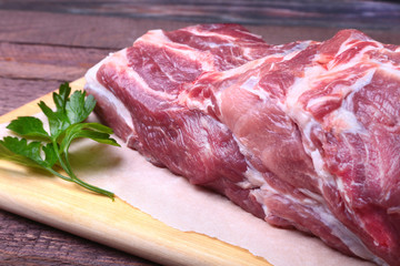 Raw pork neck chop meat with parsley herb leaves on a stone background. Ready for cooking.