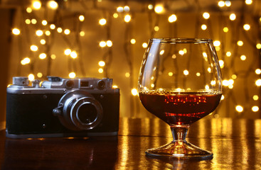 Glass of brandy or cognac and retro camera on the wooden table