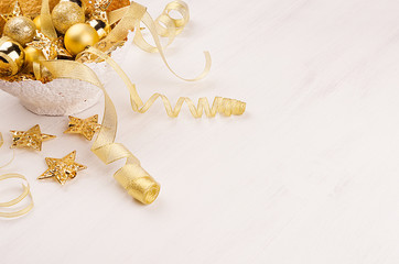Gold bowl with christmas stars, balls, ribbons on white wood board, blur. Festive xmas background.