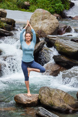 Woman in yoga asana Vrikshasana tree pose at waterfall outdoors