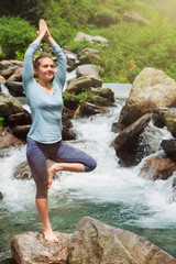 Woman in yoga asana Vrikshasana tree pose at waterfall outdoors