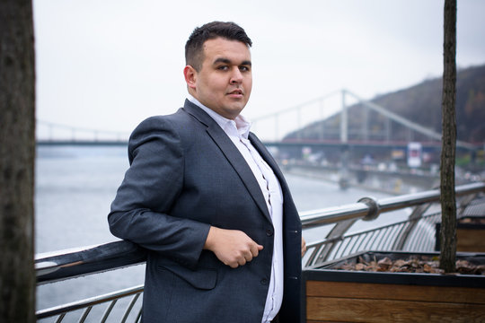 Young plus size man relaxing and enjoying the view city, plump people concept, one in big city life. Image of overweight businessman at downtown