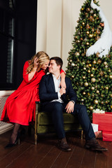 Portrait of a beautiful couple on a christmas tree background. New Year, red dress, blue business suit.