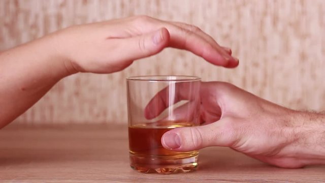 Woman pulling out a glass with whiskey from man's hands