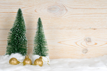 two evergreen fir trees and golden xmas baubles, snowy christmas composition, wooden background, copy space