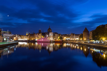 Fototapeta na wymiar Scenic view of the Motlawa River and lit old buildings on the Long Bridge waterfront at the Main Town (Old Town) in Gdansk, Poland, in the evening. Copy space.
