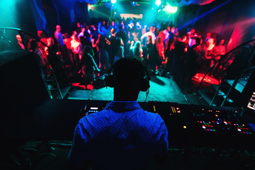 silhouette of DJ playing music on mixer and a lot of people dancing in nightclub on stage