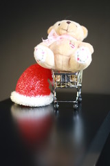 Cute fluffy teddy bear lay over mini trolley, coins and word of December sign on it, isolated on black background. Black Friday, Christmas saving and saving plan concept.