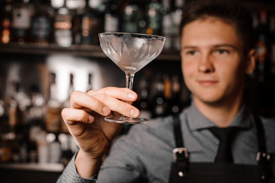 Young male barman holding a clear cocktail glass