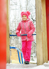 Obraz na płótnie Canvas Little girl wearing bright pink clothes on the playground outdoors in winter park