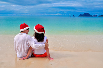 Happy couple in Santa hats relaxing on tropical sandy beach near sea, Christmas and New Year holiday romantic vacation
