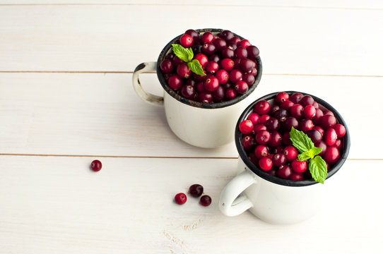 Fresh red cranberries with mint leaves in a white cup on a white wooden background. Berry background, healthy food, red berry.