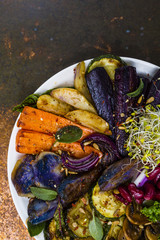 Baked and raw vegetables with herbs served on white plate.