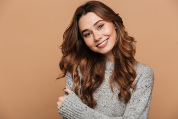Close-up portrait of cheerful brunette woman in gray knitted sweater looking at camera, isolated on beige background