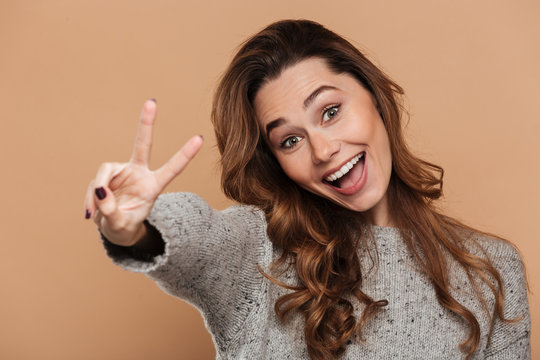 Young smiling  curly woman having fun while showing peace gesture