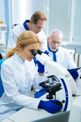 Making a discovery. Attractive serious young researcher working with a microscope while making an analysis and two male scientist working in the background
