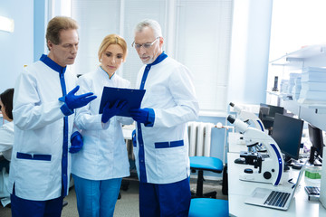 Analysing test results. Concentrated serious professional biologists wearing labcoats and discussing gene analysis results while being in the lab