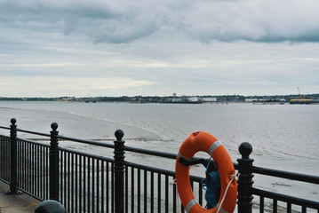 Cobbled paved footpath walkway promenade enbankment along black metal fence with orange lifebuoy at Liverpool Albert Dock.