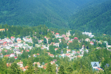Panorama of Carpathian mountains scenery, fir forest, Sinaia town village and Orthodox Sinaia Monastery on summer sunny day, a view from cableway cabin.