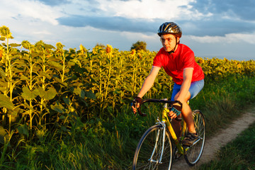 The cyclist in red blue form rides along fields of sunflowers. In background a beautiful blue sky.