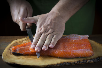Cocinero cortando lonchas de salmón en salazón para marinar y preparar sushi y otras comidas