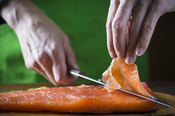 Cocinero cortando lonchas de salmón en salazón para marinar y preparar sushi y otras comidas