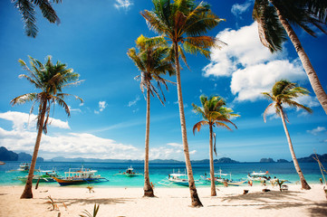 Tropical beach with palm trees, pilippine boats, blue sky, turquoise water and white sand. Paradise. Philippines, Palawan, El Nido. Wide angle, horizontal