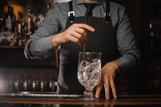 Barman in the apron stirring ice cubes with help of spoon