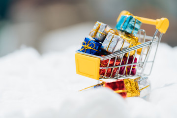 Miniature people: small gift on shopping cart with white snow. Christmas Holiday decorative concept.