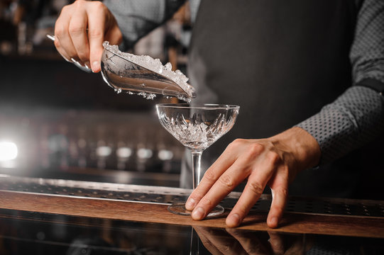Barman hand putting ice into the cocktail glass