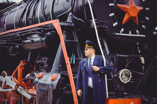 European or American train conductor is on his duty on a platform and other trains. Railway, steam trains, vintage trains .Train controller on the train, near a locomotive