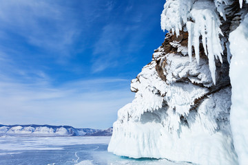 Baikal Lake in sunny winter day. Beautiful long icicles are seen on the coastal rocks